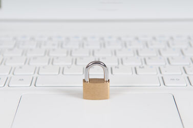 Symbolische Darstellung von Datenschutz: Vorhängeschloss auf weißem Laptop