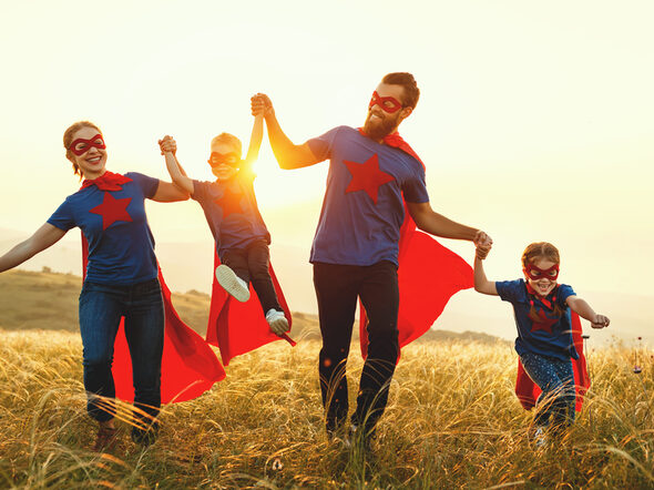 Familie als Superhelden verkleidet rennen übers Feld