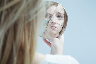 Ein Mädchen schaut in zerbrochenen Spiegel; von hinten fotografiert