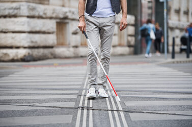 Ein Mann mit Blindenstock geht über eine Straße.