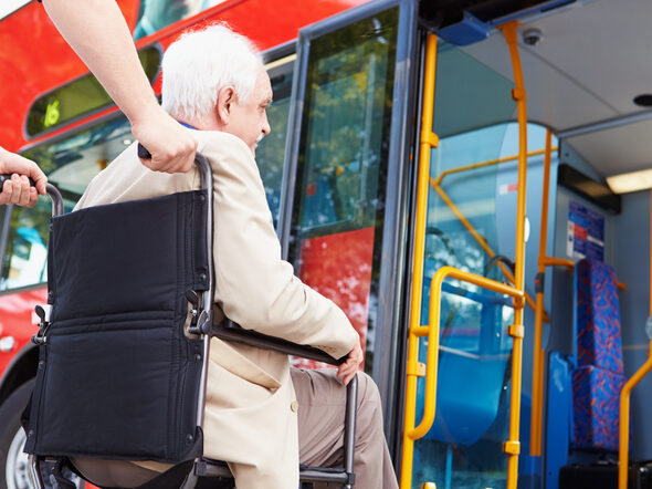 Ein Senior wird in einem Rollstuhl in einen Linienbus geschoben.