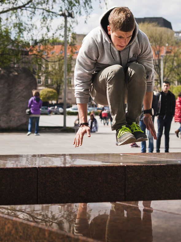 Jugendlicher springt in der Hocke über ein Hindernis in der Stadt.