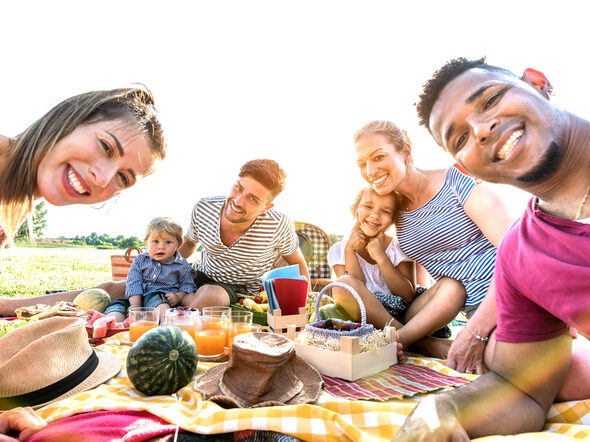 Eine Familie sitzt bei Sonnenschein auf einer Picknick-Decke.