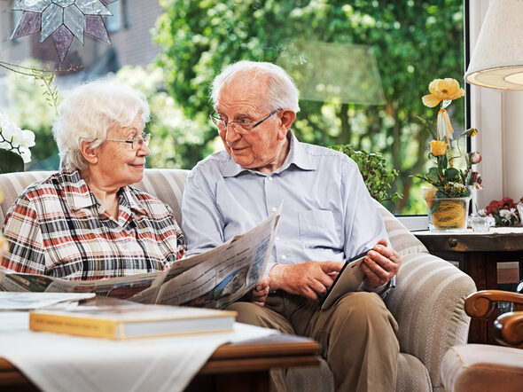 Ein älteres Ehepaar sitzt auf einem Sofa. Beide lesen.