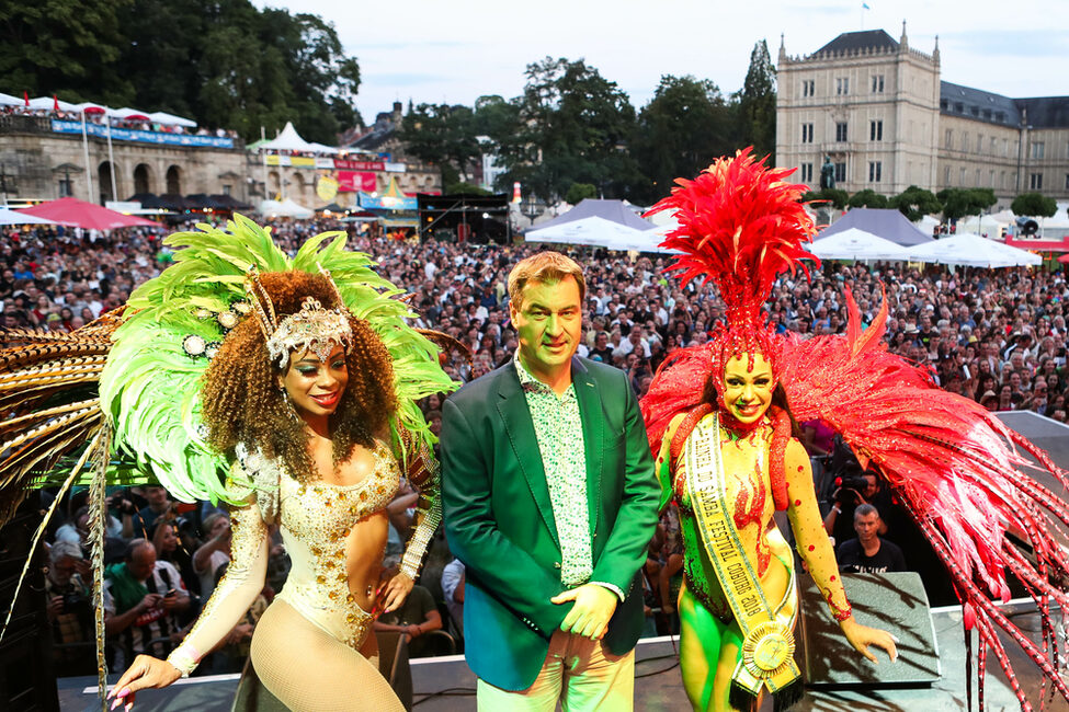 Ministerpräsident Markus Söder auf der Bühne des Sambafestivals, umringt von zwei Samba-Tänzerinnen