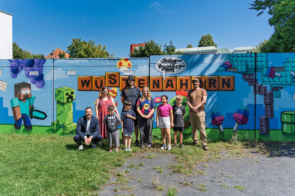 Bürgermeister Can Aydin, das Team des KiJuz zusammen mit den jungen Künster*innen vor ihrem Graffiti in Wüstenahorn.