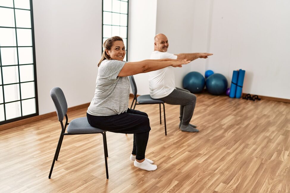 Middle,Age,Hispanic,Couple,Stretching,Using,Chair,At,Sport,Center.