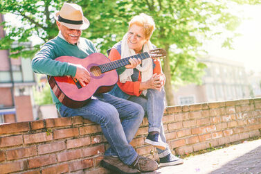 Happy,Senior,Couple,Playing,A,Guitar,While,Sitting,Outside,On