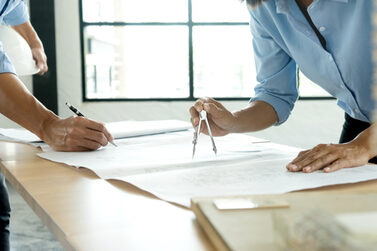 Zwei Architekten zeichnen mit Zirkel auf einen großen Plan