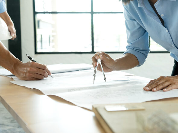 Zwei Architekten zeichnen mit Zirkel auf einen großen Plan