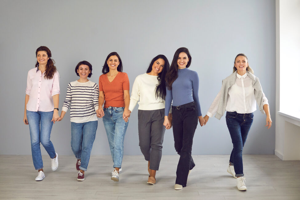 Eine Gruppe junger fröhlicher Frauen laufen in einer Reihe auf die Kamera zu und halten sich an den Händen
