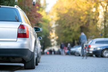 Auto parkt am Straßenrand, im Hintergrund Verkehrsteilnehmer