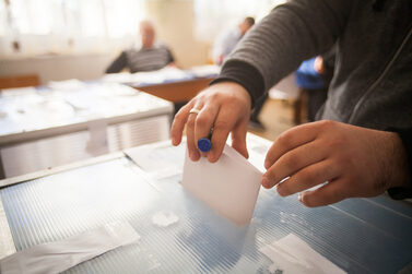 Eine Person wirft einen Stimmzettel in eine Wahlurne