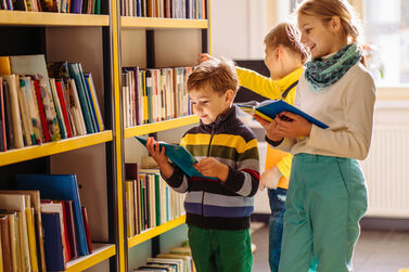 Ein Mädchen und zwei Jungen schauen sich Bücher in einer Bücherei an.