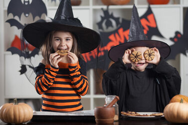 Zwei Kinder in Hexenkostümen präsentieren ihre selbst gemachten Halloween-Kekse.