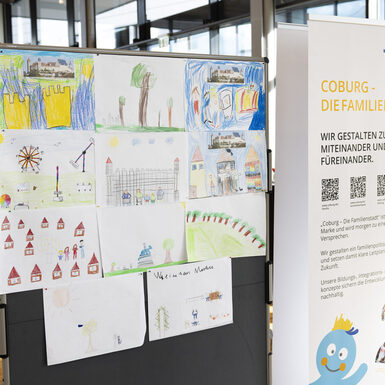 Gemalte Bilder von Kinder an einer Stellwand mit Informationen zur Familienstadt daneben