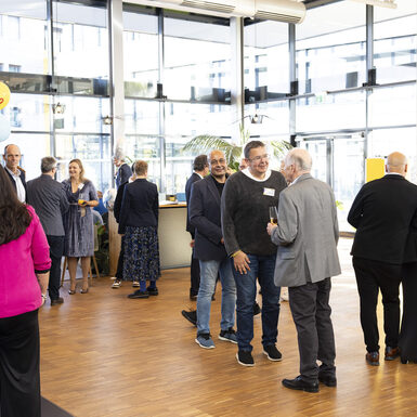 Mehrere Personen stehen in Gruppen an Stehtischen und unterhalten sich