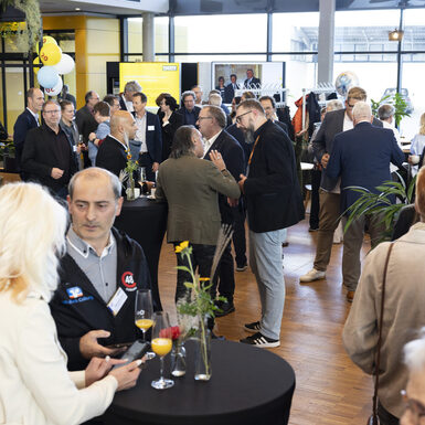 Mehrere Personen stehen in Gruppen an Stehtischen und unterhalten sich