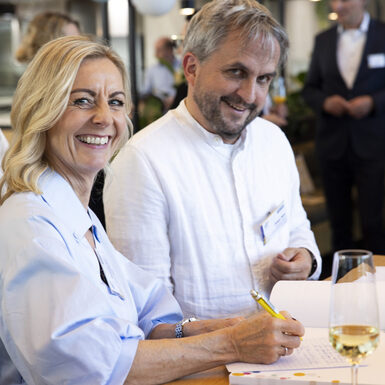 Eine Dame und Herren schreiben in ein Gästebuch und lachen in die Kamera