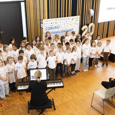 Schülerinnen udn Schüler stehen vor einem Klavier.