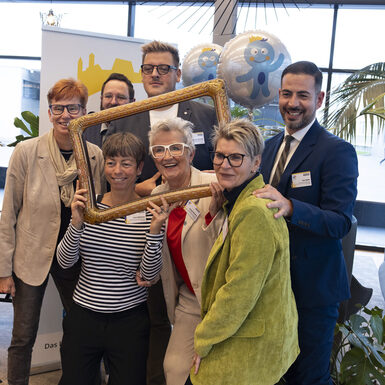 Mehrere Personen schauen durch einen Rahmen. Von ihnen wird ein gemeinsames Bild gemacht.