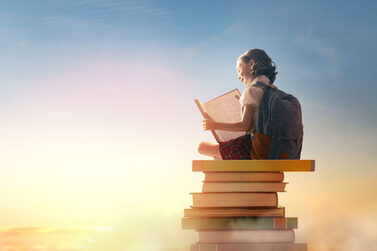 Kind sitzt auf einem Bücherstapel