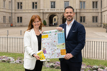 Bianca Haischberger und 3. Bürgermeister Can Aydin präsentieren den Kinderstadtplan vor der Ehrenburg