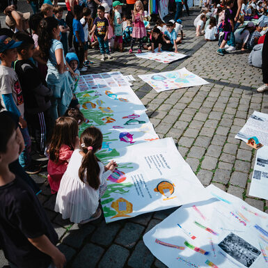 Eine Gruppe von Kindern steht oder sitzen zusammen rund um selbstgestaltete Plakate zum Thema Toleranz
