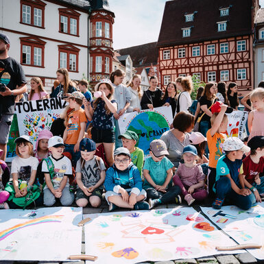 Kinder sitzen auf dem Boden rund um selbstgestaltete Plakate zum Thema Toleranz oder halten Plakate in ihren Händen