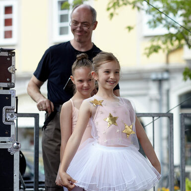 Zwei Mädchen in Ballettkleidung stehen hintereinander und lachen.