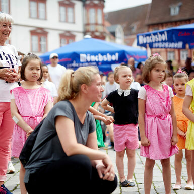 Eine Gruppe von Kindern steht beieinander und schaut in die gleiche Richtung. Eine Frau kniet vor den Kindern.