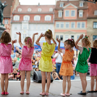 Eine Gruppe von Kindern in bunten Kostümen steht auf der Bühne und tanzt.