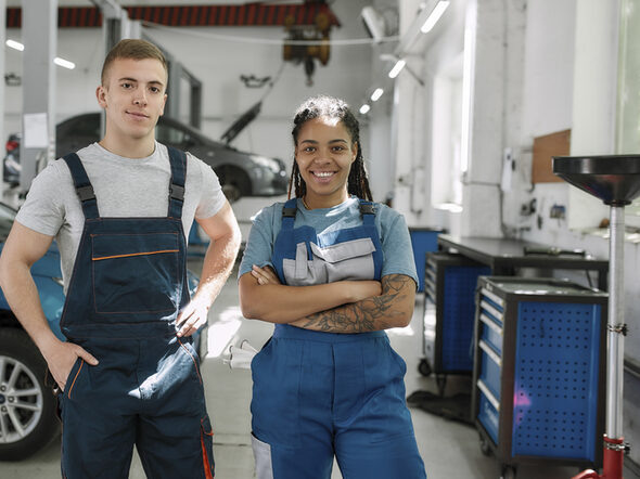 Zwei Auszubildende in einer Autowerkstatt schauen in die Kamera