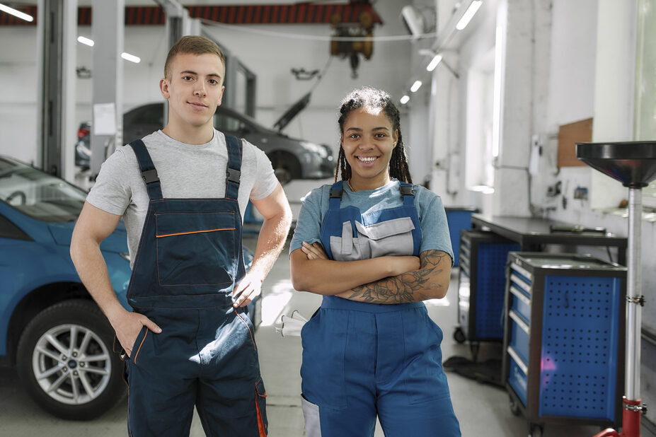 Zwei Auszubildende in einer Autowerkstatt schauen in die Kamera