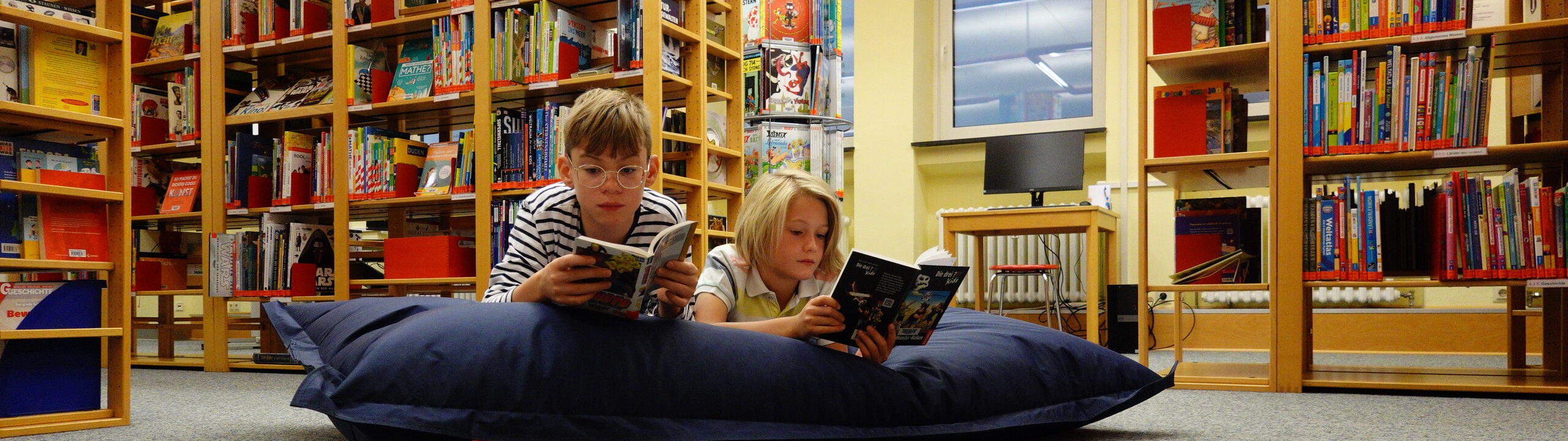 Zwei Jungen liegen mit Büchern in der Hand auf einem Sitzsack in der Kinder- und Jugendbücherei