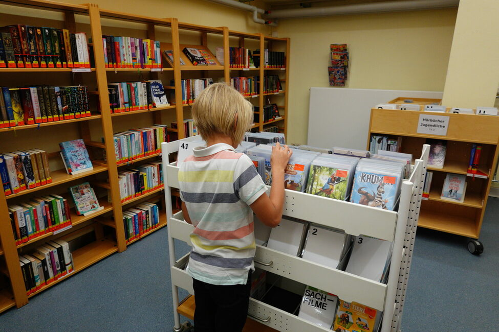 Ein Junge durchsucht DVD in einem Regal der Kinder- und Jugendbücherei