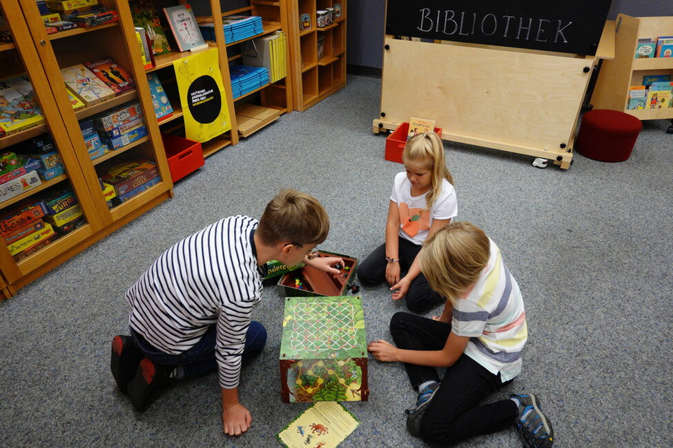 Kinder spielen auf dem Boden der Kinder- und Jugendbücherei ein Gesellschaftsspiel