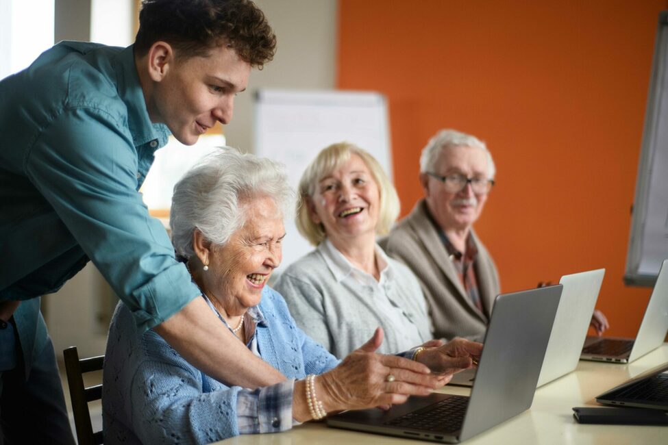 Jugendlicher hilft Senior*innen am Laptop